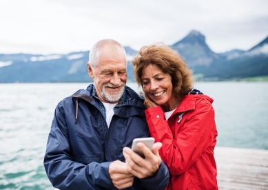 older couple in the outdoors taking a selfie with mountains and a lake in the background